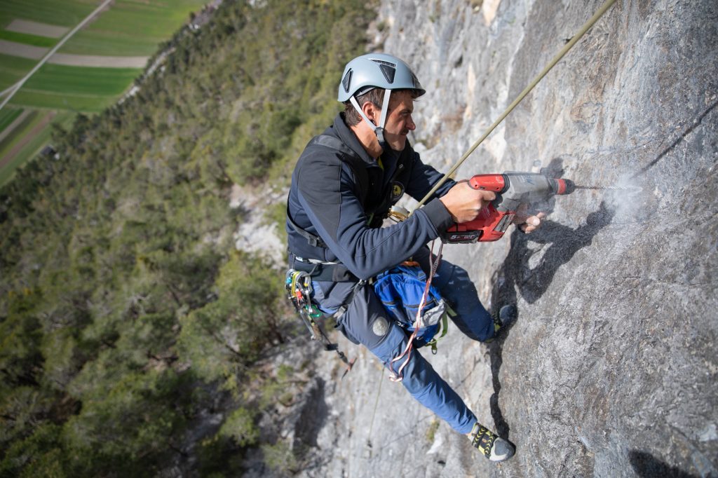 Das Bild zeigt einen Kletterer beim Bohren in einer Felswand.