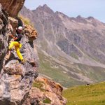 Das bild zeigt einen Kletterer mit gelber Hose auf einer grauen Felswand.