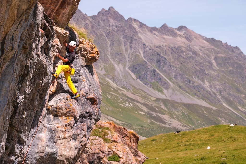 Das bild zeigt einen Kletterer mit gelber Hose auf einer grauen Felswand.