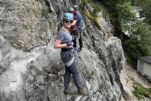 Eine Frau klettert, gesichert durch ein Stahlseil und ihrem Klettersteiggurt an einem Klettersteig am Achensee