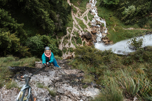 Eine Frau klettert, gesichert durch ein Stahlseil und ihrem Klettersteiggurt an einem steilen Klettersteig am Achensee