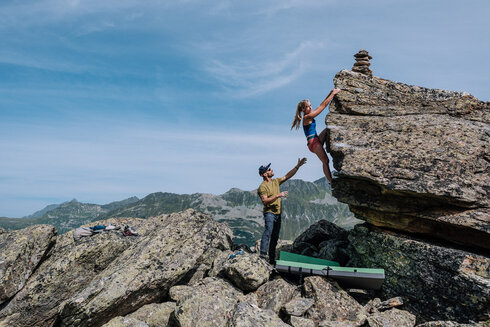 Eine Frau bouldert am Felsen. Der Kletterer spottet die Sportlerin von unten. 