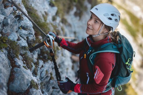 Eine junge Frau klettert einen Klettersteig und sichert sich mit einem Sicherungsset für Klettersteiggeher