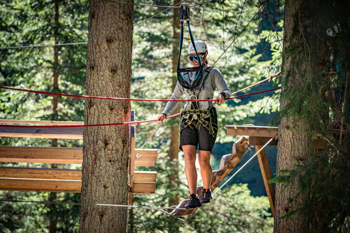 eine Frau balanciert über eine Seilbrücke in einem Waldseilgarten am Arlberg