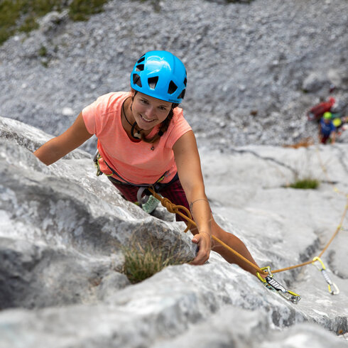 Eine Frau klettert an einer Felswand, trägt einen blauen Helm und ist in voller Kletterausrüstung