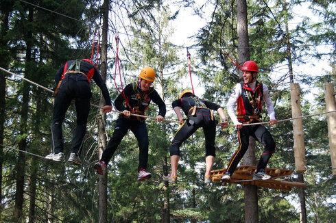 Climbers cross a rope bridge that requires balance. 