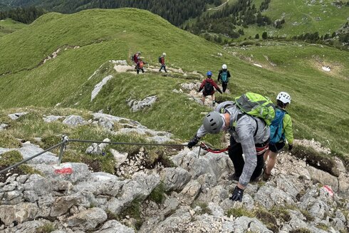 Eine Klettergruppe klettert, gesichert durch ein Stahlseil und ihrem Klettersteiggurt an einem Klettersteig am Achensee