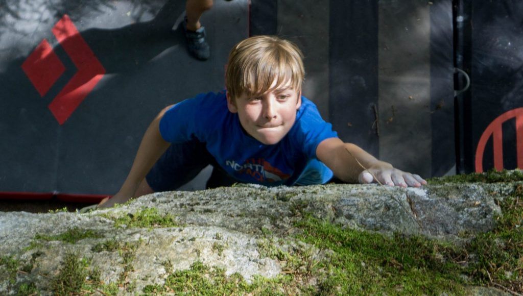 Kind bouldert auf einem Felsblock