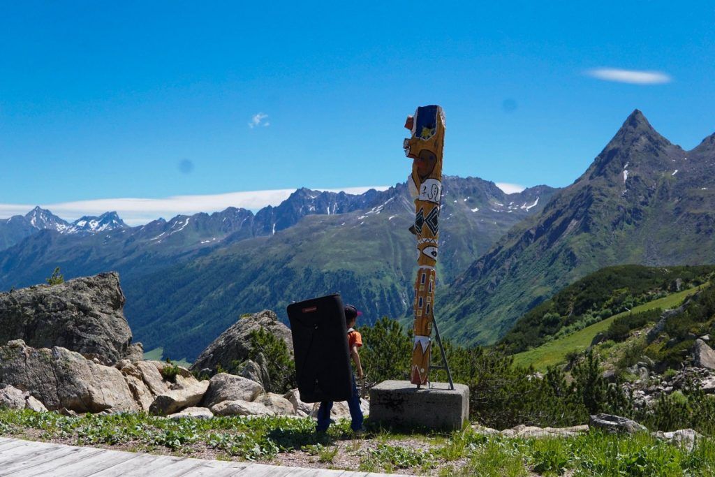 Kind klettert an einer Felswand, im Hintergrund Berglandschaft