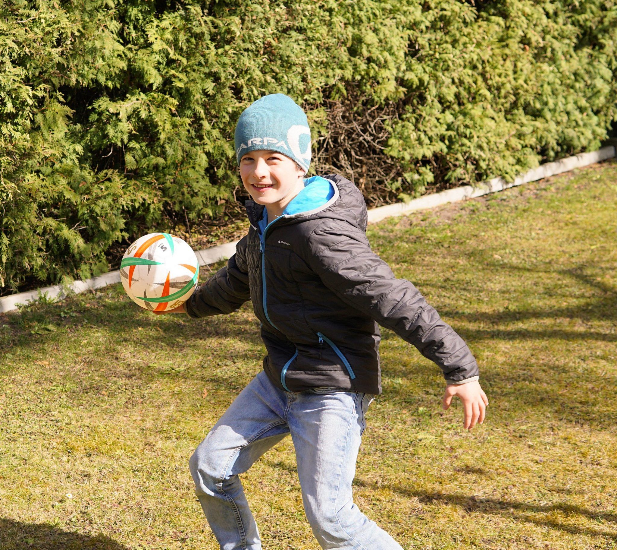 Ein Kind mit Mütze wirft auf einer Wiese einen Ball