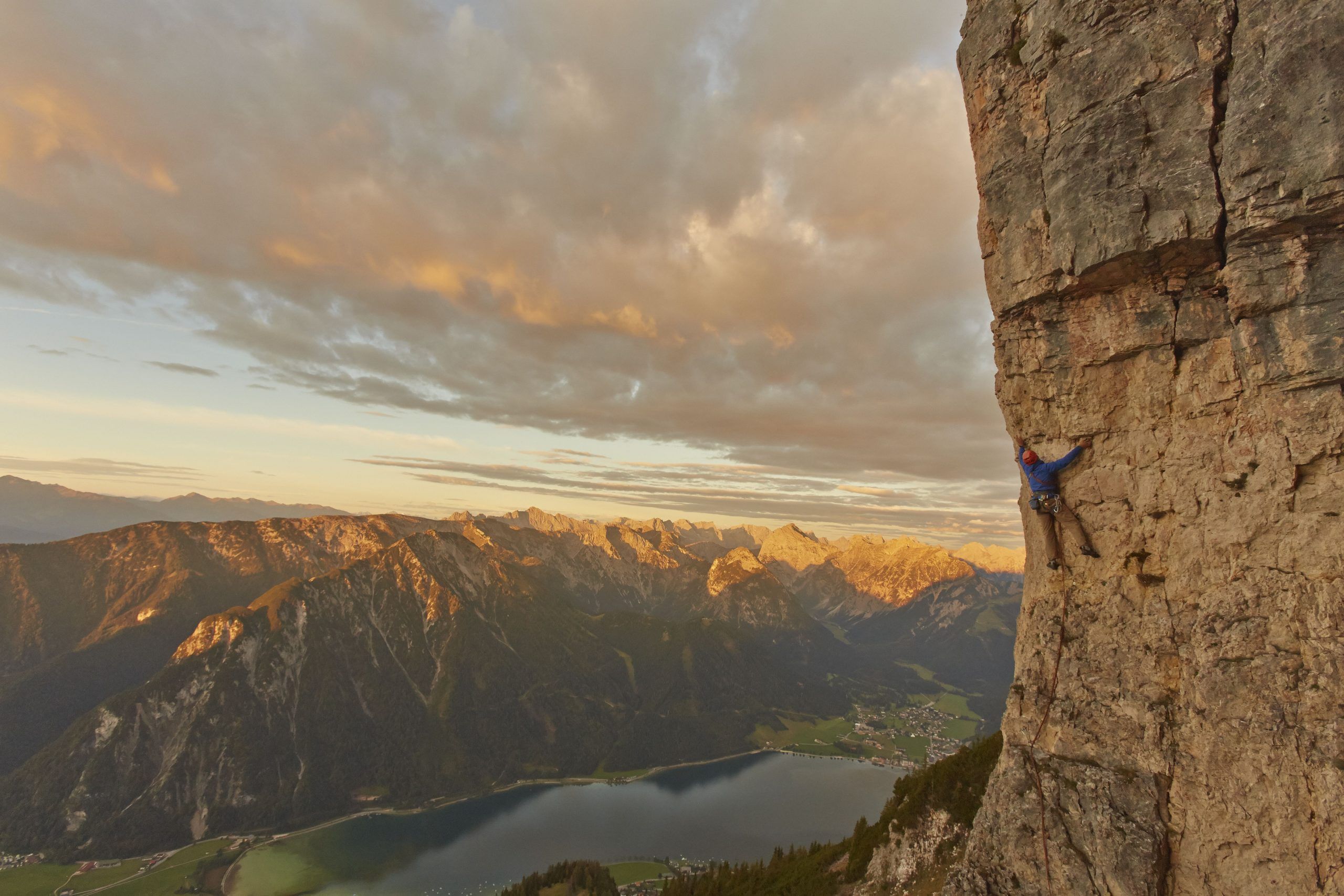 Kletterin in einer Felswand im Rofan mit Blick auf den Achensee in der Abendsonne