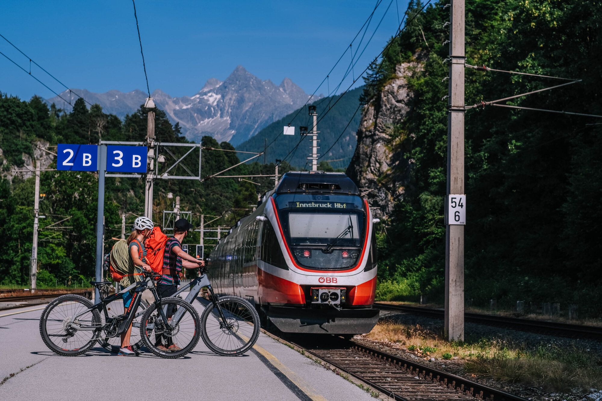 einfahrender Zug und wartende Fahrradfahrer am Bahnhof