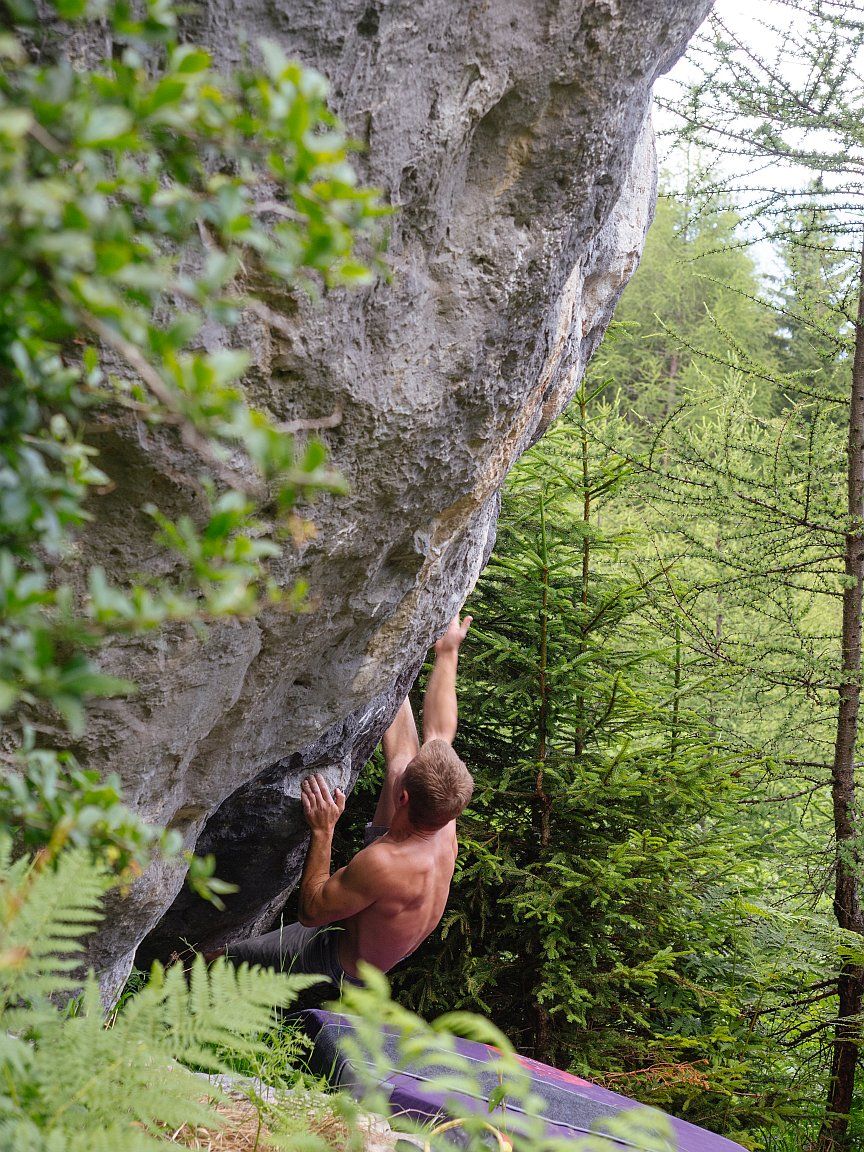 A boulderer on a boulder in the forest high above Imst