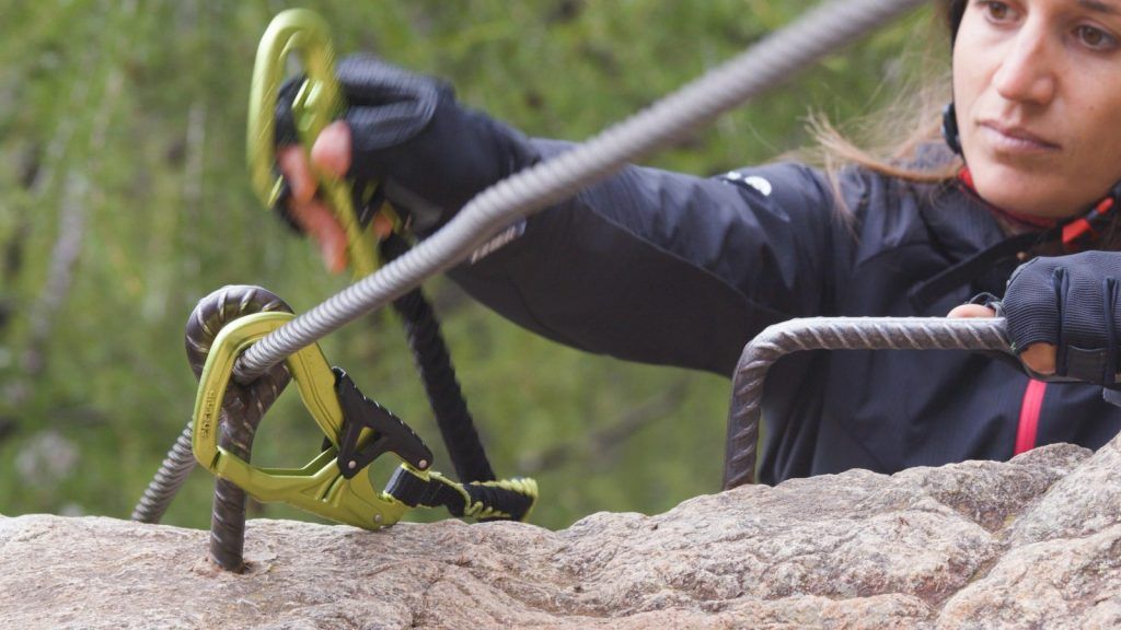 A hand opens a via ferrata carabiner with a palm-lock mechanism