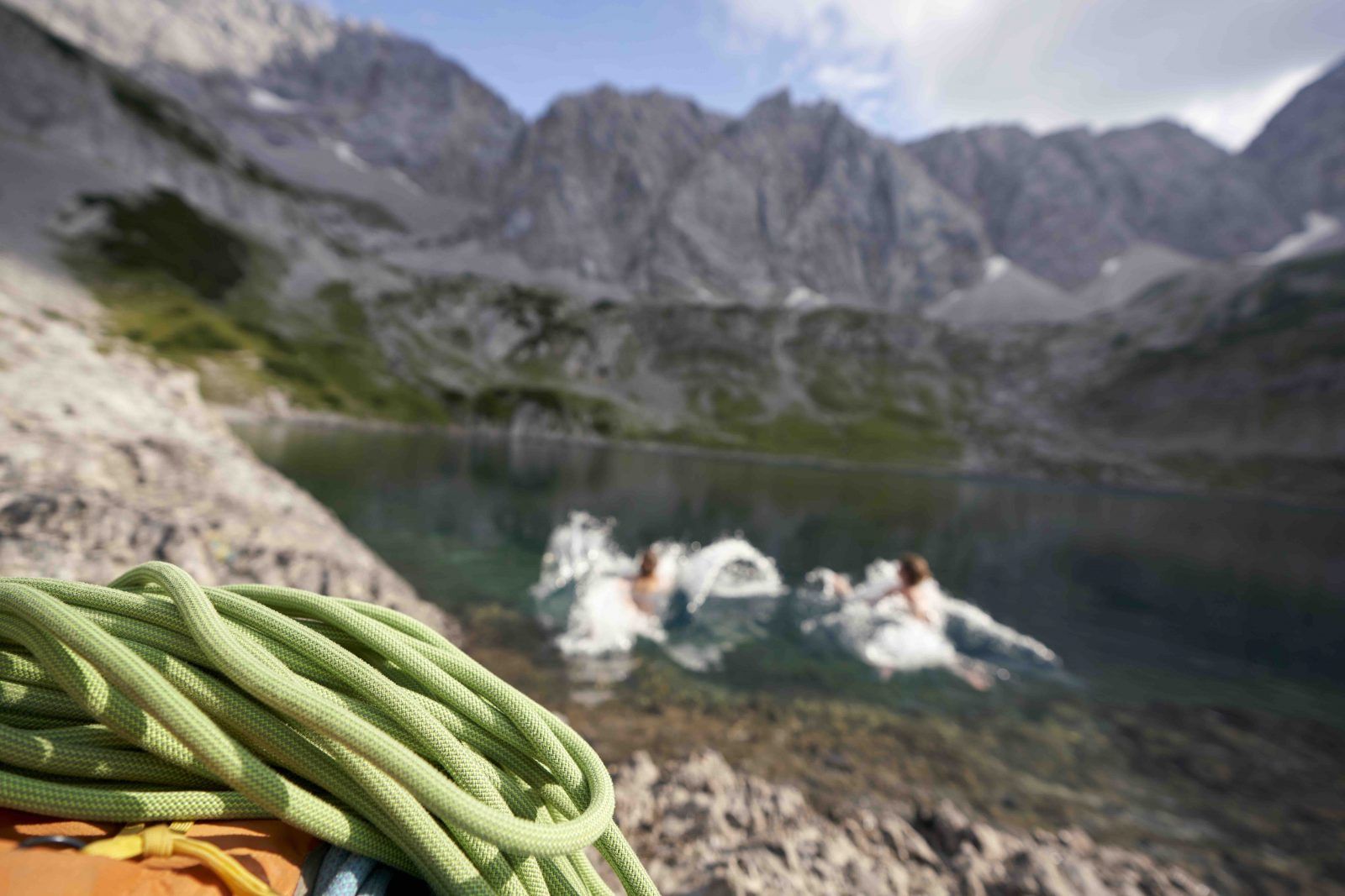Kletterseil am Ufer des Seebensees, dahinter drei Frauen beim Baden im Bergsee