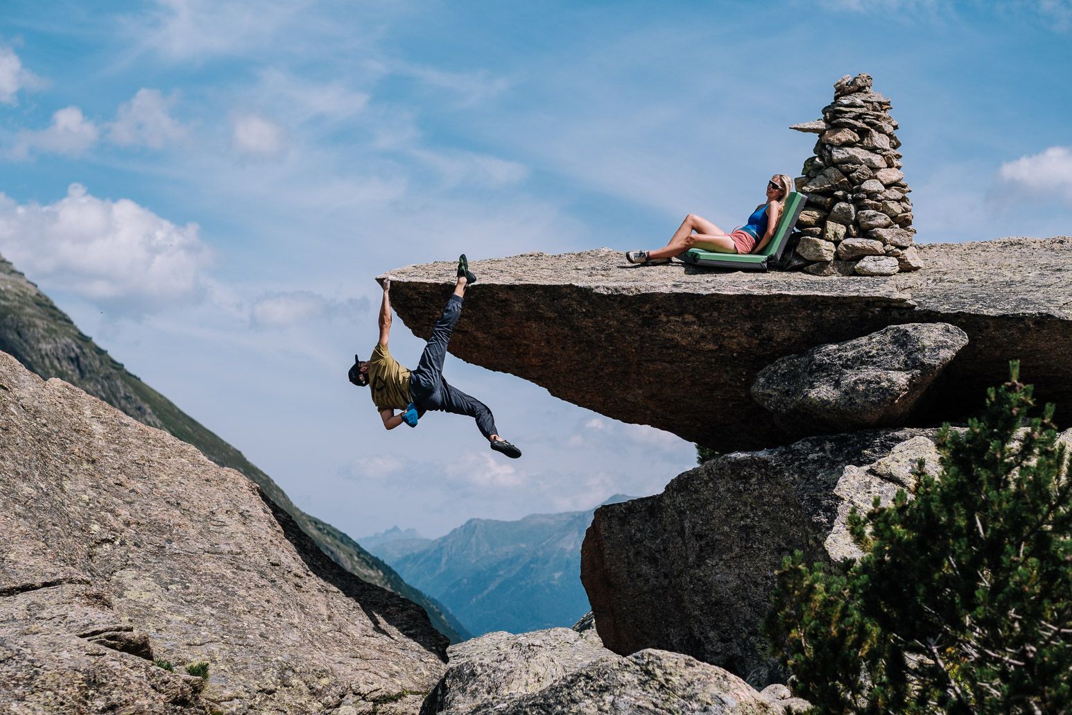 Ein Mann hängt einarmig von einem Felsen.