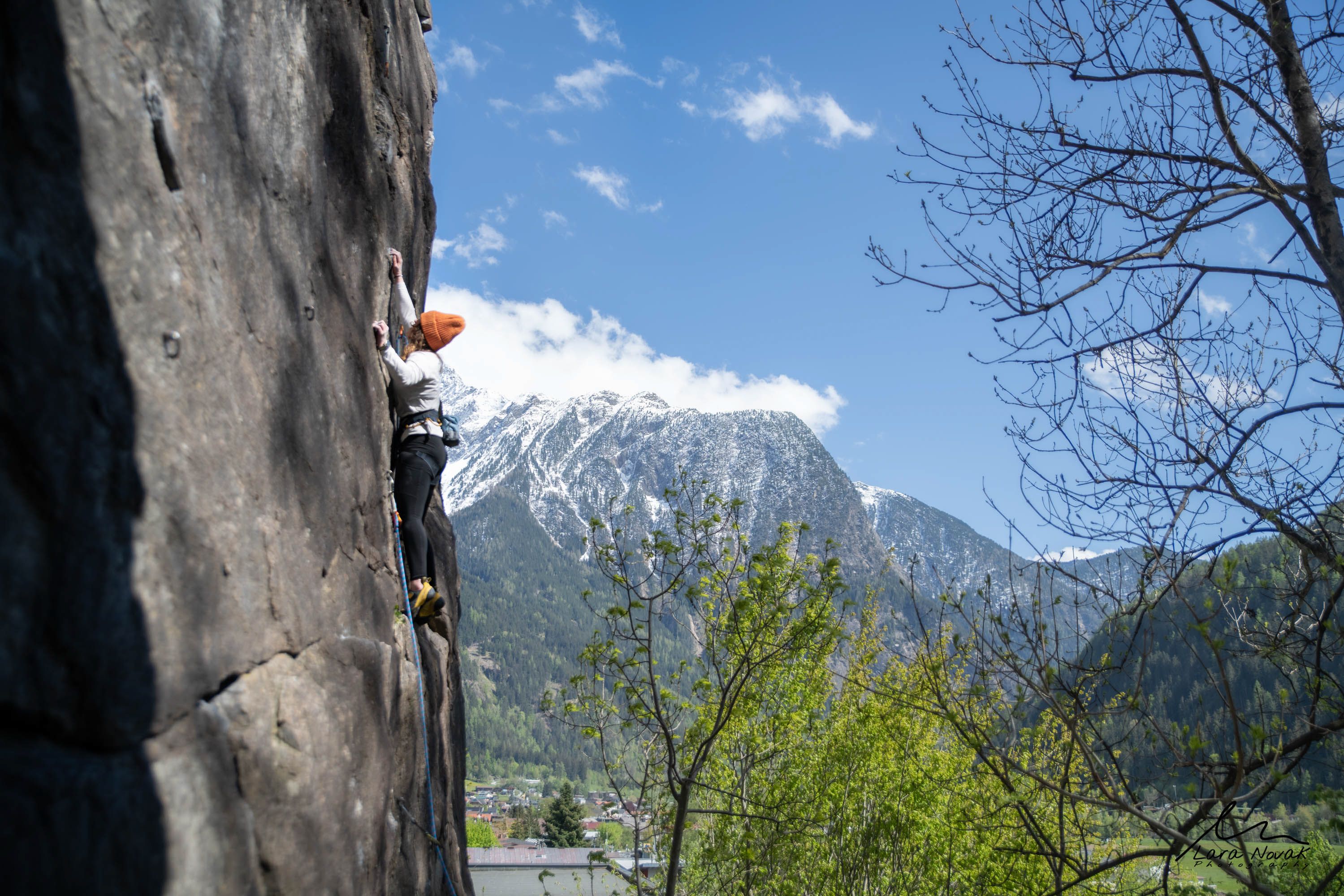 Kletterer an einer Felswand im Klettergarten Oetz, im Hintergrund verschneite Berge und blauer Himmel